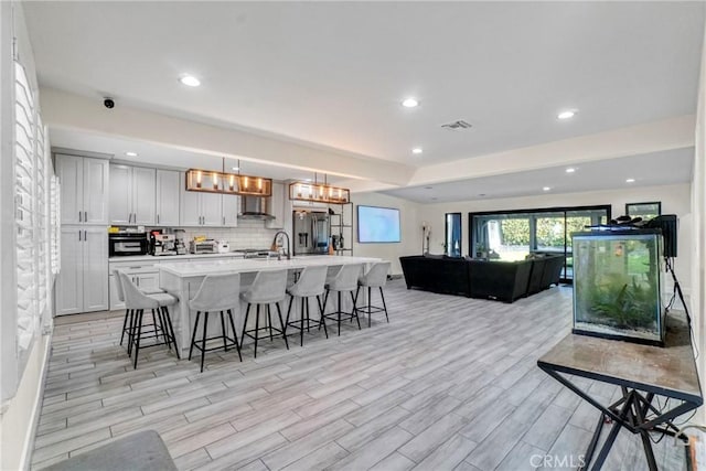kitchen with visible vents, stainless steel refrigerator with ice dispenser, a kitchen breakfast bar, open floor plan, and light countertops