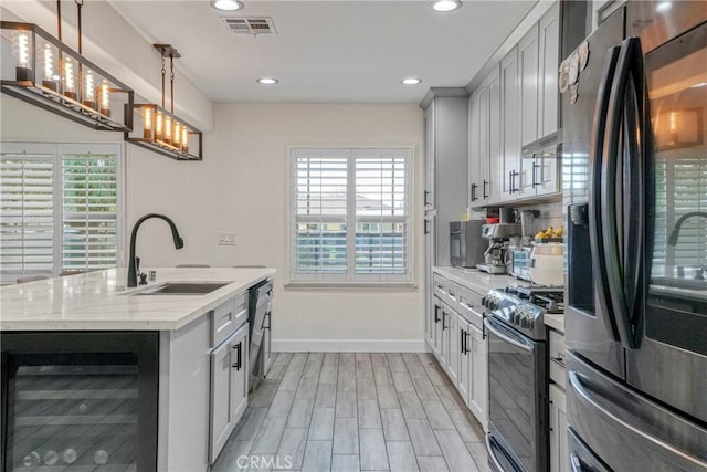 kitchen with beverage cooler, stainless steel appliances, sink, hanging light fixtures, and light stone counters