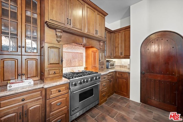 kitchen featuring designer stove, backsplash, and light stone countertops