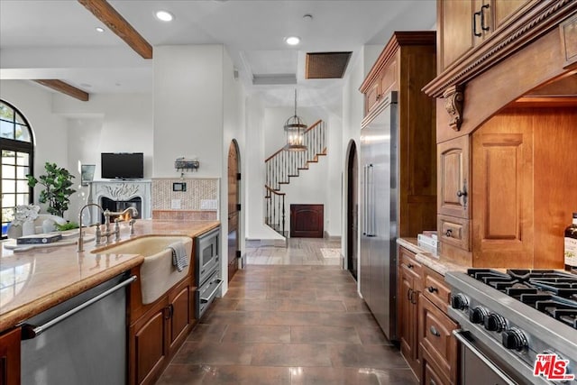 kitchen featuring a notable chandelier, beam ceiling, decorative backsplash, sink, and built in appliances