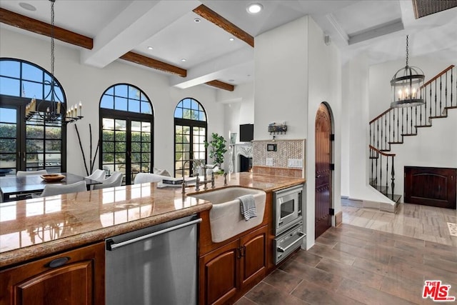 kitchen featuring appliances with stainless steel finishes, a notable chandelier, hanging light fixtures, beam ceiling, and sink