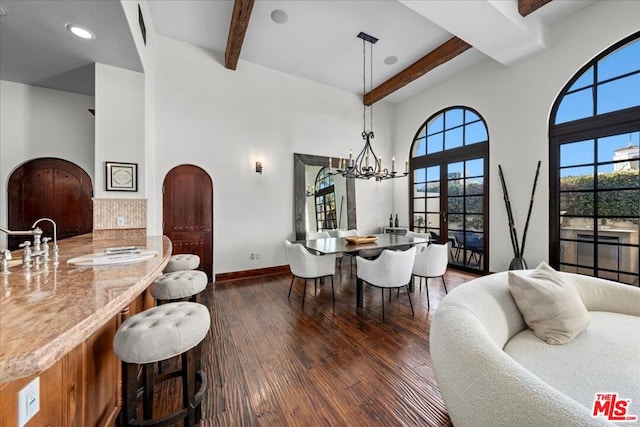 dining space with a high ceiling, dark hardwood / wood-style floors, a notable chandelier, and beamed ceiling