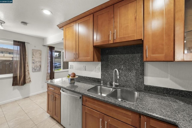 kitchen with stainless steel dishwasher, tasteful backsplash, dark stone countertops, sink, and light tile patterned floors