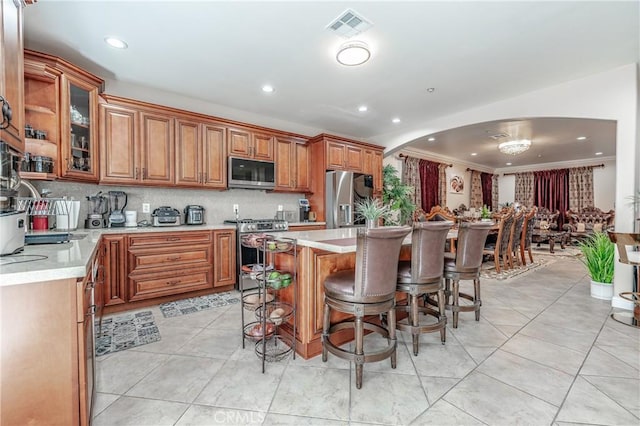 kitchen with a breakfast bar area, a center island, light tile patterned floors, appliances with stainless steel finishes, and backsplash