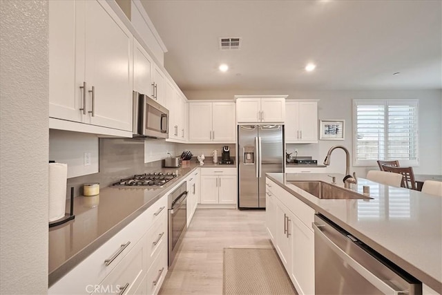 kitchen featuring appliances with stainless steel finishes, sink, white cabinets, and light hardwood / wood-style flooring