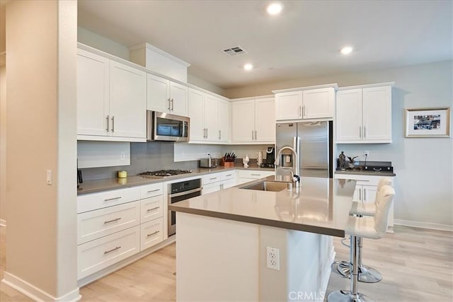 kitchen with stainless steel appliances, an island with sink, sink, and white cabinetry