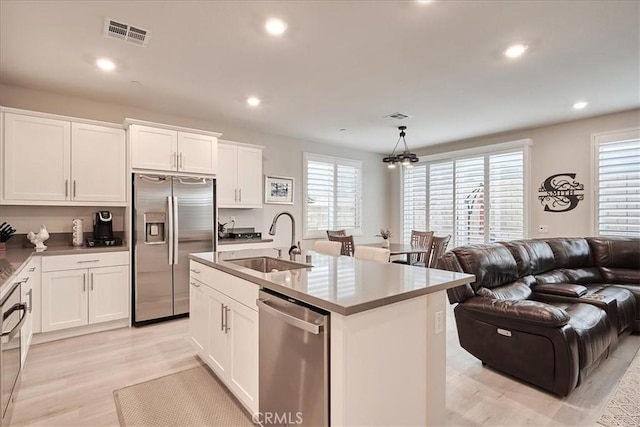 kitchen featuring pendant lighting, sink, white cabinetry, stainless steel appliances, and a center island with sink