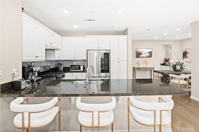 kitchen featuring white cabinetry, appliances with stainless steel finishes, dark stone countertops, light hardwood / wood-style flooring, and sink