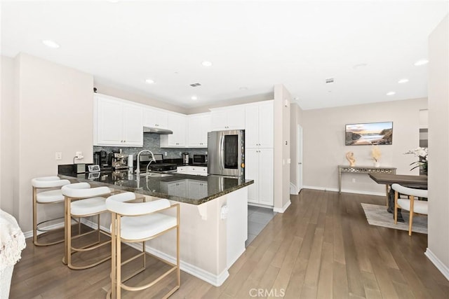 kitchen with kitchen peninsula, dark hardwood / wood-style flooring, appliances with stainless steel finishes, white cabinets, and dark stone counters