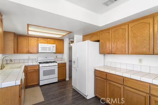 11636 Kerrie Way, Apple Valley, CA 92308 - kitchen with white appliances, a sink, dark wood-style flooring, tile counters, and brown cabinets