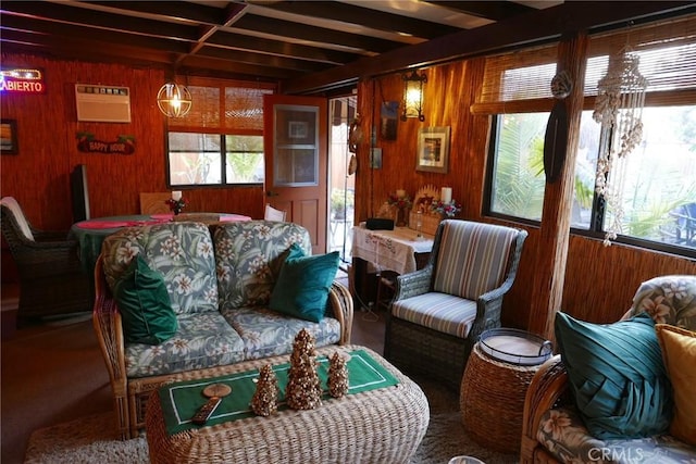 living room featuring a healthy amount of sunlight, a wall mounted air conditioner, wooden walls, and beamed ceiling