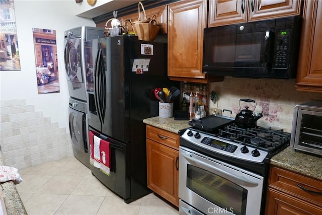 kitchen featuring stone counters, light tile patterned flooring, stacked washer / dryer, tasteful backsplash, and black appliances