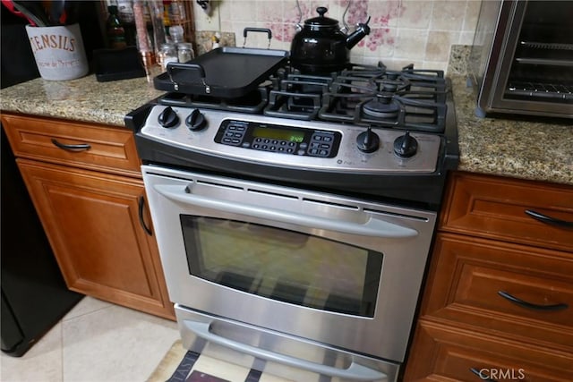 kitchen with light tile patterned flooring, stainless steel range with gas stovetop, light stone countertops, and backsplash