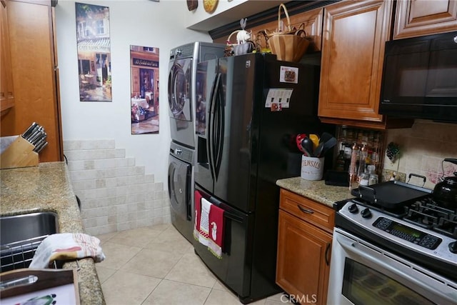 kitchen with decorative backsplash, stacked washer and dryer, light tile patterned floors, light stone counters, and black appliances