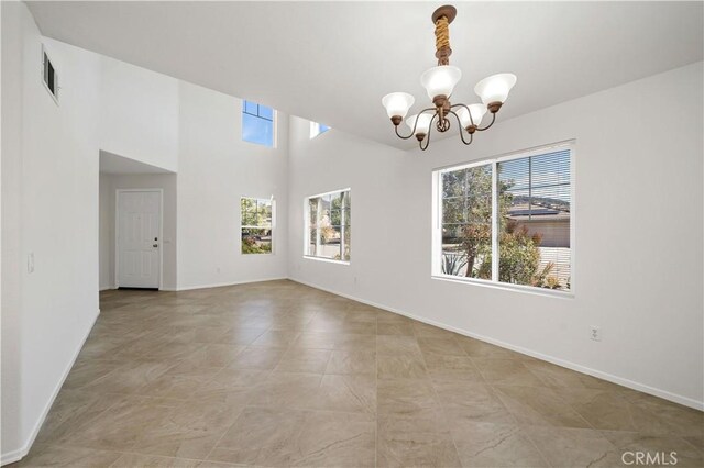 spare room featuring a healthy amount of sunlight, a notable chandelier, and a towering ceiling