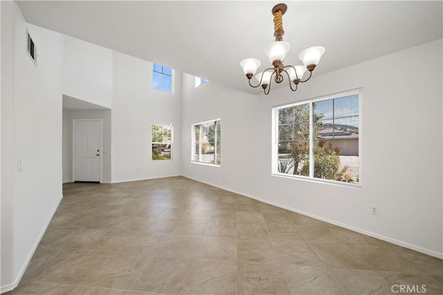 unfurnished room featuring a high ceiling, plenty of natural light, and a chandelier