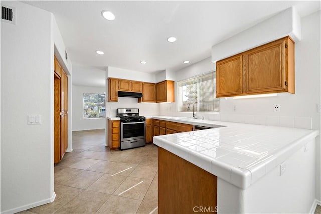 kitchen featuring stainless steel gas stove, a wealth of natural light, tile counters, and kitchen peninsula