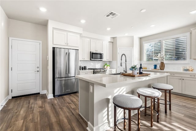 kitchen featuring a kitchen bar, sink, a center island with sink, appliances with stainless steel finishes, and white cabinets