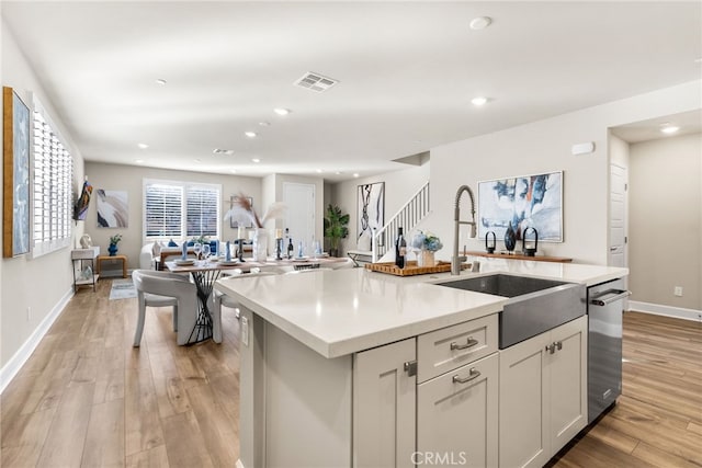 kitchen with dishwasher, sink, white cabinets, a center island with sink, and light wood-type flooring