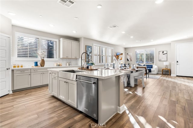 kitchen with dishwasher, sink, a center island with sink, and light hardwood / wood-style flooring