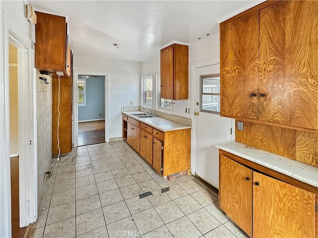 kitchen with tile countertops, brown cabinetry, light tile patterned flooring, and a sink