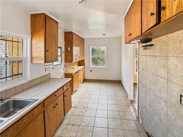 kitchen featuring light tile patterned floors, baseboards, tile counters, brown cabinets, and a sink