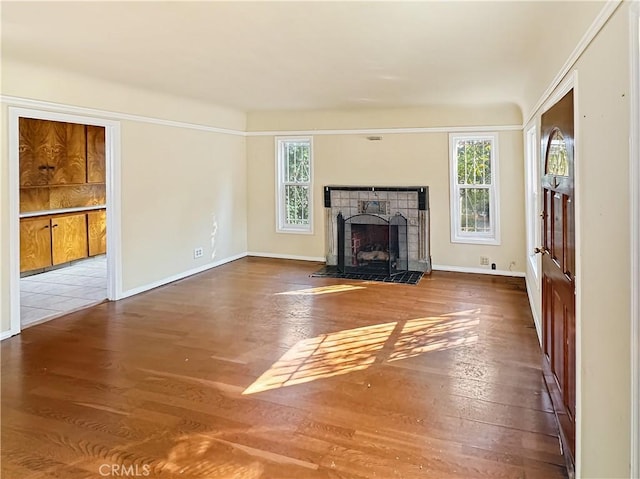 unfurnished living room featuring a tile fireplace, plenty of natural light, baseboards, and wood finished floors