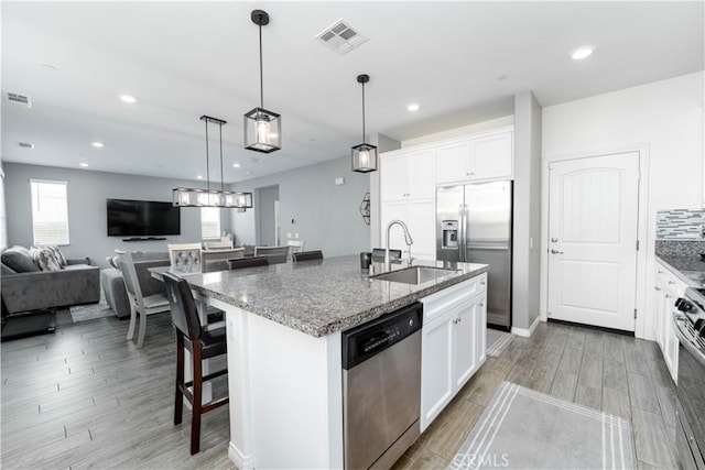 kitchen featuring sink, white cabinetry, a kitchen island with sink, stainless steel appliances, and dark stone counters