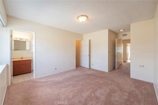 unfurnished bedroom featuring connected bathroom, light colored carpet, and a textured ceiling