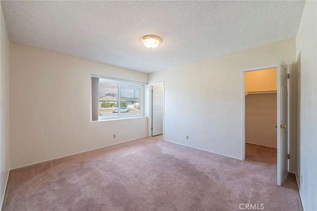 unfurnished bedroom featuring a spacious closet, light colored carpet, and a textured ceiling