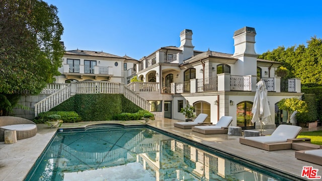 back of property featuring a fenced in pool, a balcony, and a patio