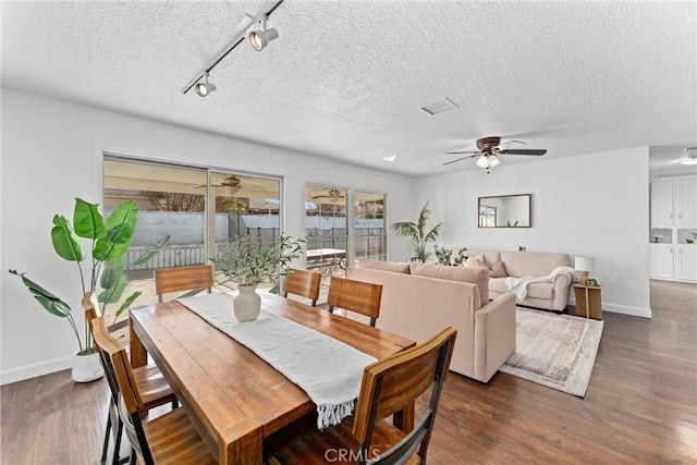 dining space with ceiling fan, track lighting, dark hardwood / wood-style floors, and a textured ceiling