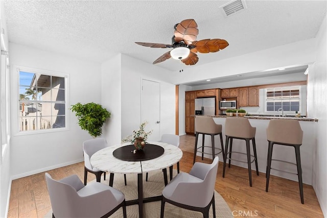 dining area with ceiling fan, sink, a textured ceiling, and light hardwood / wood-style floors