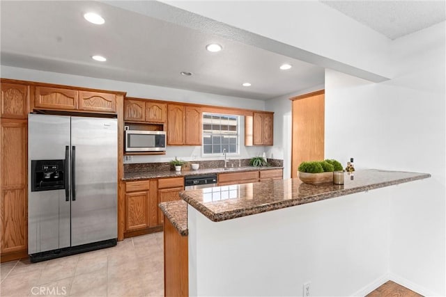 kitchen featuring sink, dark stone countertops, light tile patterned floors, kitchen peninsula, and stainless steel appliances