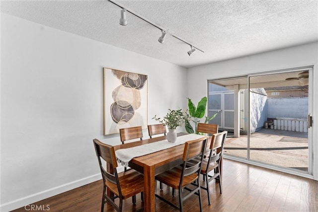 dining room featuring dark wood-type flooring, track lighting, and a textured ceiling