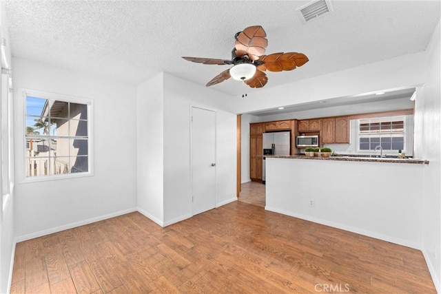 unfurnished living room featuring ceiling fan, light hardwood / wood-style floors, sink, and a textured ceiling