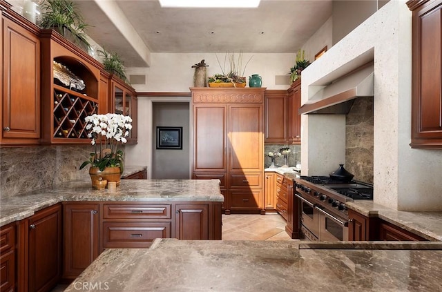 kitchen featuring light stone countertops, wall chimney exhaust hood, decorative backsplash, and range with two ovens