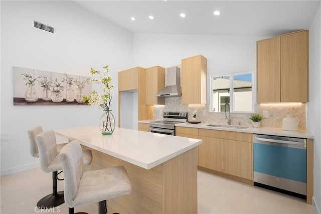 kitchen with a kitchen island, sink, appliances with stainless steel finishes, light brown cabinetry, and wall chimney exhaust hood