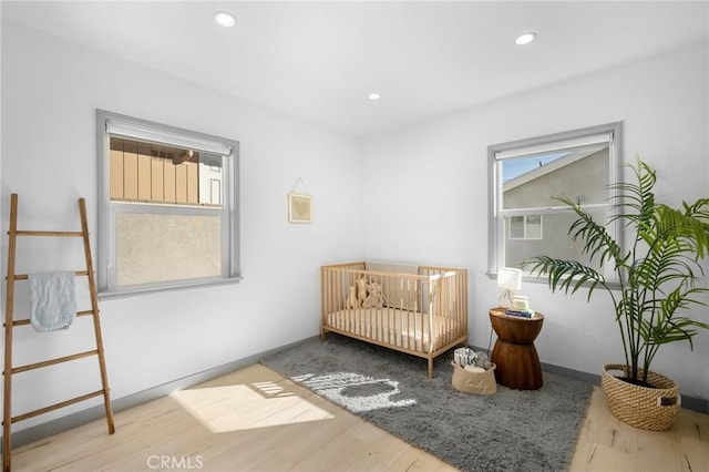 bedroom featuring multiple windows, hardwood / wood-style floors, and a crib