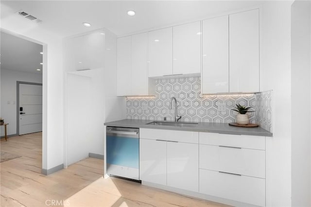 kitchen featuring tasteful backsplash, stainless steel dishwasher, sink, light hardwood / wood-style flooring, and white cabinets