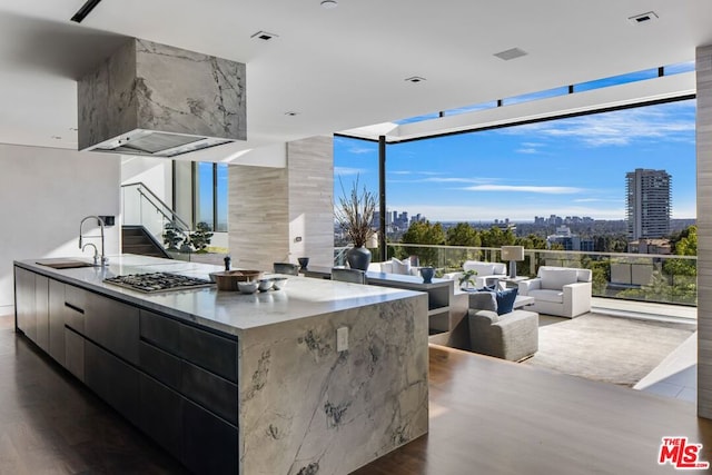 kitchen featuring stainless steel gas stovetop, a spacious island, sink, dark wood-type flooring, and wall chimney exhaust hood