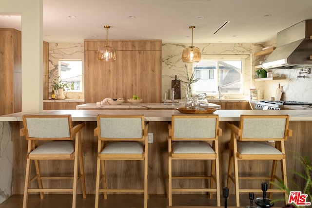 kitchen with a kitchen bar, wall chimney exhaust hood, and pendant lighting