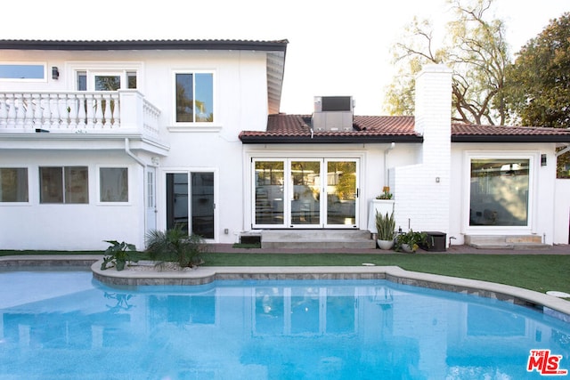 rear view of property featuring a lawn, central air condition unit, and a balcony