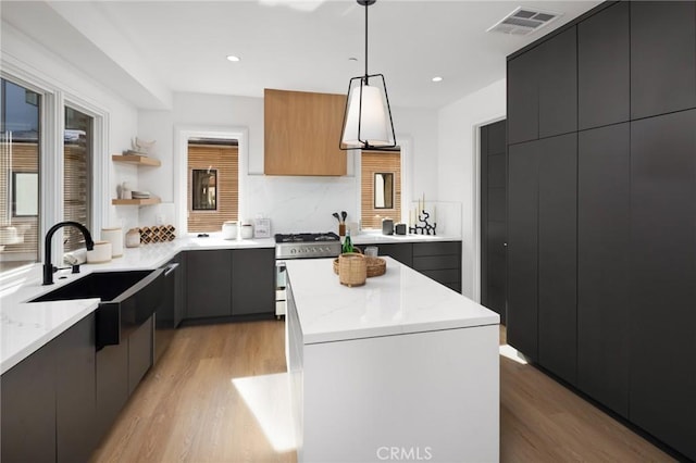 kitchen with white gas stove, light hardwood / wood-style flooring, hanging light fixtures, and a center island