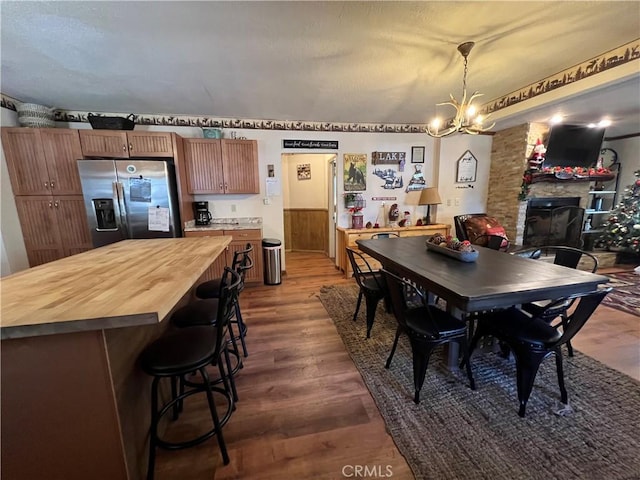 dining area with dark wood-type flooring, a stone fireplace, and a notable chandelier