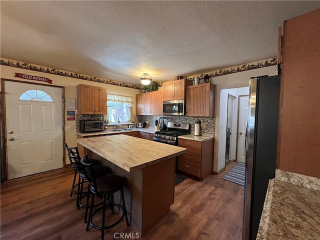 kitchen with wooden counters, a kitchen island, a breakfast bar, sink, and stainless steel appliances