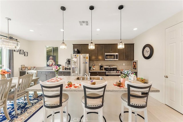 kitchen featuring a kitchen bar, appliances with stainless steel finishes, sink, dark brown cabinets, and an island with sink