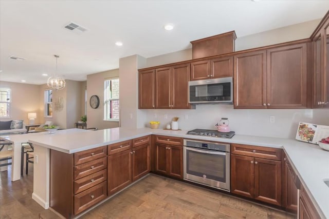 kitchen featuring decorative light fixtures, kitchen peninsula, appliances with stainless steel finishes, and hardwood / wood-style floors