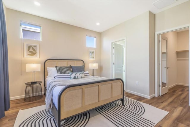 bedroom with multiple windows, a walk in closet, and hardwood / wood-style floors