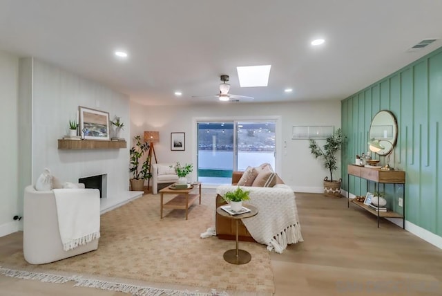 living room featuring a fireplace, a skylight, ceiling fan, and light wood-type flooring